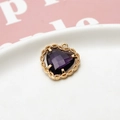 Macro view of heart-shaped purple zircon pendant with gold lace border on white ceramic - Deep purple