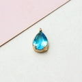 Makroaufnahme eines hellblauen Kristallanhängers in Tropfenform mit goldenem Sockel - 6x11mm / Seeblau