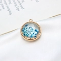 Détail macro d'un pendentif rond doré avec fleurs séchées bleues pour création de bijoux - 22mm / Bleu