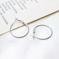 Macro shot of silver metal hoop earrings with pin closure on a white textured background - 25mm / White Gold