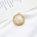 Vue macro d'un pendentif rond doré avec fleur séchée blanche dans de la résine - 22mm / Blanc