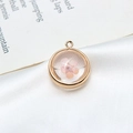 Vue macro d'un pendentif rond doré avec fleur séchée rose sur de la soie blanche - 18mm / Rose