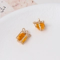 Detailed macro of golden gift box earrings with amber yellow crystal and bow detail - Yellow