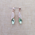 Détail macro de boucles d'oreilles or rose avec cristaux blancs et pierres vertes en forme de feuille - Or Vert