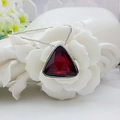 Detailed macro view of a dark red triangular faceted crystal pendant with a silver bezel - Red