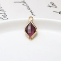 Close-up of a gold-plated rhombus drop pendant with purple faceted glass on white ceramic - Deep purple