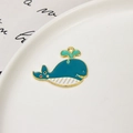Detail shot of a blue whale-shaped alloy charm with green water drops and gold plating - Whale