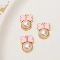 Macro detail of pink enamel bow pendants with imitation pearl on white ceramic tray - Pink