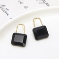 Close-up of black crystal padlock earrings in golden setting on a white ceramic plate - Stud Earrings / Black