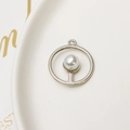 Close-up of a silver round pearl pendant on a white ceramic tray with gold decor - Silver Round Style