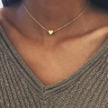 Detail of minimalist gold heart pendant necklace on a fine chain worn by a model - Gold