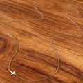 Detailed view of silver cross chain with lobster clasp on dark wood background - Gold