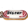 Vue macro d'un pendentif capsule en acier inoxydable avec texte Sister et accents rouges - Lettre Ovale