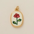 Vue détaillée d'un pendentif ovale doré avec broderie de rose rouge sur fond blanc - Pendentif Fleur de Novembre