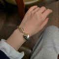 Gouden hartvormige hanger armband met OT-sluiting getoond om de pols van een vrouw - Gouden Armband