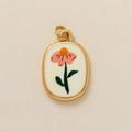 Detailopname van een ovale gouden hanger met roze bloemenvormig borduurwerk en bladaccenten - April Bloem Hanger