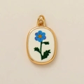 Detail van een ovale gouden hanger met blauwe bloem op wit geëmailleerd paneel - Februari Bloem Hanger