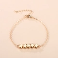 Minimalistische gouden sterrenarmband met vijf bedeltjes op een roze achtergrond - Goud
