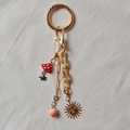 Detail of gold keychain with mushroom, peach, sun mask charms and acrylic chain - Sun Peach Bag Chain