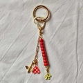 Detail of colorful keychain with pink heart, gold bee, and red bead flower on white fabric - Bee And Flower Charm