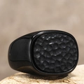 Makroaufnahme eines schwarzen Titanrings für Herren mit Hammerschlag-Textur auf Stein - Schwarz