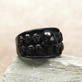 Detail of a black punk skull ring with 3D embossed skulls on a textured stone surface - US 7 / Black