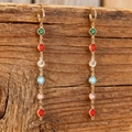 Detalle de pendientes largos dorados con gemas de colores colgados sobre madera - Pendientes
