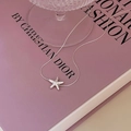 Detailweergave van een zilveren zeester hanger ketting op een zachte lavendel boekomslag - Zeester Ketting