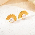 Detailed view of golden sunburst fan earrings with pearls on white stone display - Fan Pearl Earrings