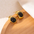 Detailed close-up of golden irregular teardrop earrings with black oval gemstone on wood - Black Amber