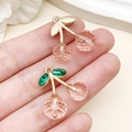 Pendentifs cerises roses avec feuilles dorées et vertes présentés sur un doigt pour la taille - Cerise Résine Rose Translucide Strass Vert Or KC (23427) / 21x20x10mm
