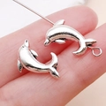 Pair of polished silver dolphin charms for DIY jewelry making on a hand background - Ocean Dolphin Spacer Bead (15981)