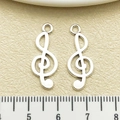 Silver treble clef music charm pendants for DIY jewelry making shown with ruler - Antique Silver Treble Clef (5619)