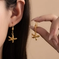 Detail of bohemian gold starfish drop earrings worn by a model in warm studio lighting - Starfish Earrings