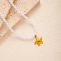 Detail einer Perlenkette mit mattem 18K Gold-Seestern-Anhänger auf einer Steinfläche - Seestern (Künstliche Perle Halskette)