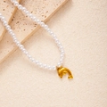 Detailansicht der goldenen Delfin-Halskette mit weißen Perlen auf einer Steinfläche - Delphin (Künstliche Perle Halskette)