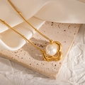 Detailed shot of a vintage gold floral pendant with large pearl on a textured stone surface - Four-petal Floral Style (JJN0077)
