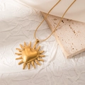 Detail of gold sun heart pendant necklace with snake chain on white pleated background - Heart Starburst Radiance (JJN0053)