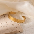 Detail of gold-plated open bangle with fine feather texture on a travertine stone base - Feather Texture Open Style (#0258)