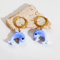 Close-up of blue gradient dolphin earrings with gold hoops on a textured stone - Blue Dolphin