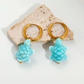 Detailed close-up of blue ceramic sea turtle earrings on a textured stone display - Light Blue Sea Turtle Shape (1425)