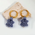 Macro detail of blue ceramic turtle charm with gold hoop earring on a natural stone surface - Dark Blue Turtle