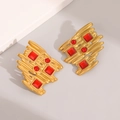 Detailed close-up of gold geometric earrings with red rhinestones on a white stand - Gold Irregular Metal Strips With Red Gemstone Style (E1676)