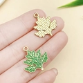 Green maple leaf enamel pendant with gold trim shown on fingertip for scale - Artemisia Leaf (23035) / 21x20mm