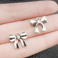 Coppia di ciondoli a fiocco in argento antico sul dito per creazione gioielli fai da te - Stile Fiocco con Laccio Argento Antico (19431)