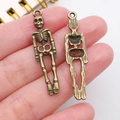 Colgantes de calavera de bronce para joyería DIY, mostrados en mano para escala - Estilo de Figura de Esqueleto (20100) / 1 Unidad (9x39mm) / Bronce Antiguo