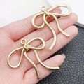 Hand holding two gold hollow bow-knot alloy pendants for DIY jewelry and bag charms - Large Bowknot (43x42mm)