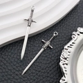 Detail of two antique silver alloy sword charms with intricate relief patterns on black leather - Antique Silver Cross Guard Sword Style