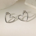 Close-up of minimalist silver heart stud earrings on a textured white aesthetic background - Hollow Heart Stud (XKE0206)