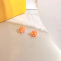 Detailed macro view of orange-pink daisy stud earrings with yellow centers on marble surface - Pink